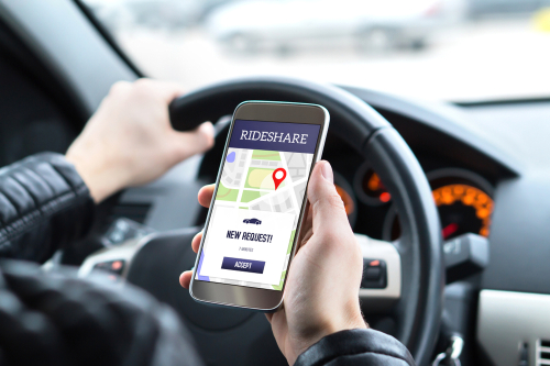 A rideshare driver holding a smartphone with the rideshare app open while driving, showing a new ride request on the screen.