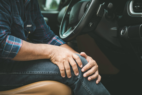 Person seated in a car holding their injured knee after an accident, showing possible leg pain.