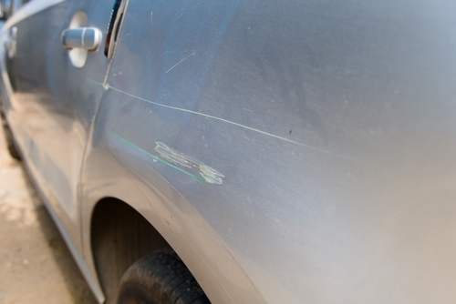 Close-up of a silver car door with visible scrape marks and paint transfer after a sideswipe.