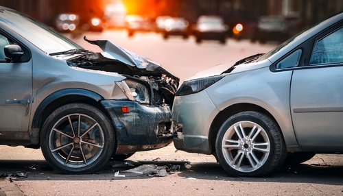 Close view of two damaged vehicles facing each other after a frontal crash on a city street at sunset.
