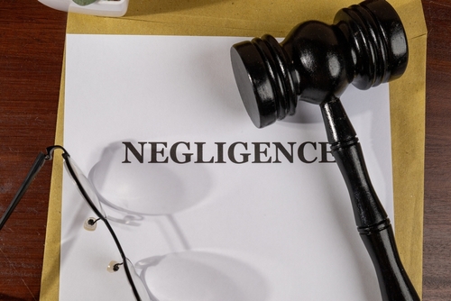 Close-up of a legal document labeled “Negligence” with a black gavel and reading glasses on a wooden desk.