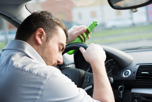 Man asleep at the wheel holding a green beer bottle, suggesting drunk driving and dangerous impaired behavior.