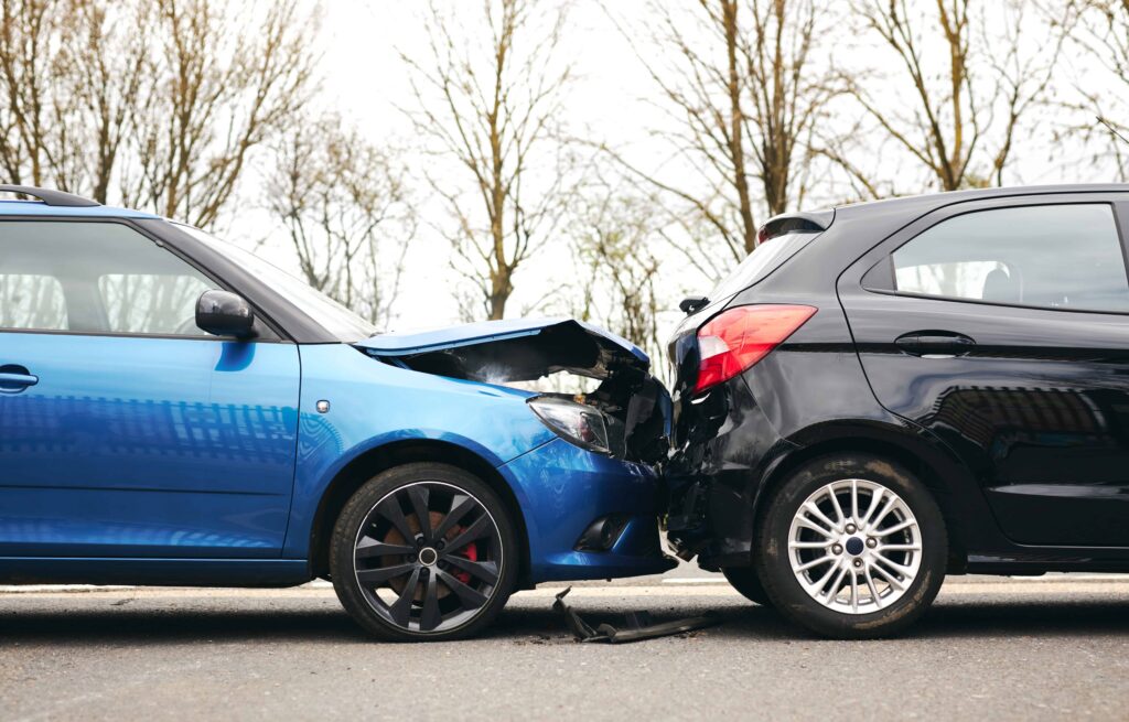 Rear-end car accident with visible damage as blue vehicle crashes into black car on road, showing collision impact. Rear-end car accident with visible damage as blue vehicle crashes into black car on road, showing collision impact.
